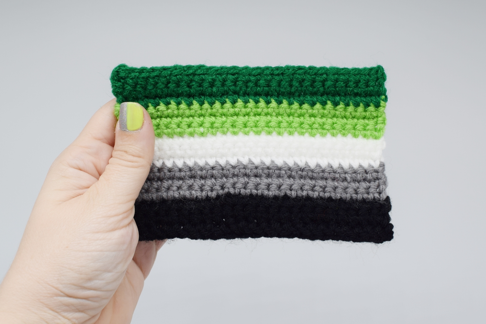 hand holding a crochet aromantic pride flag