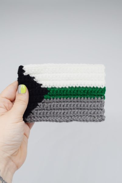 Hand holding a crochet demiromantic pride flag on a white background