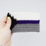 Hand holding a crochet demisexual pride flag on a white background