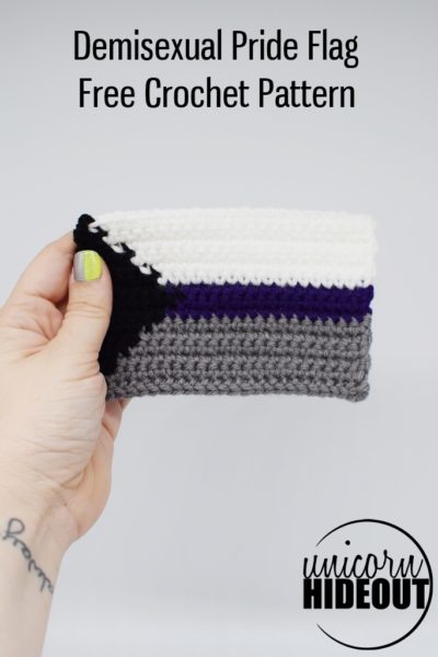 Hand holding a crochet demisexual pride flag on a white background, words on image: "Demisexual Pride Flag Free Crochet Pattern Unicorn Hideout"