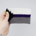 Hand holding a crochet demisexual pride flag on a white background