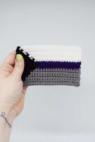 Hand holding a crochet demisexual pride flag on a white background