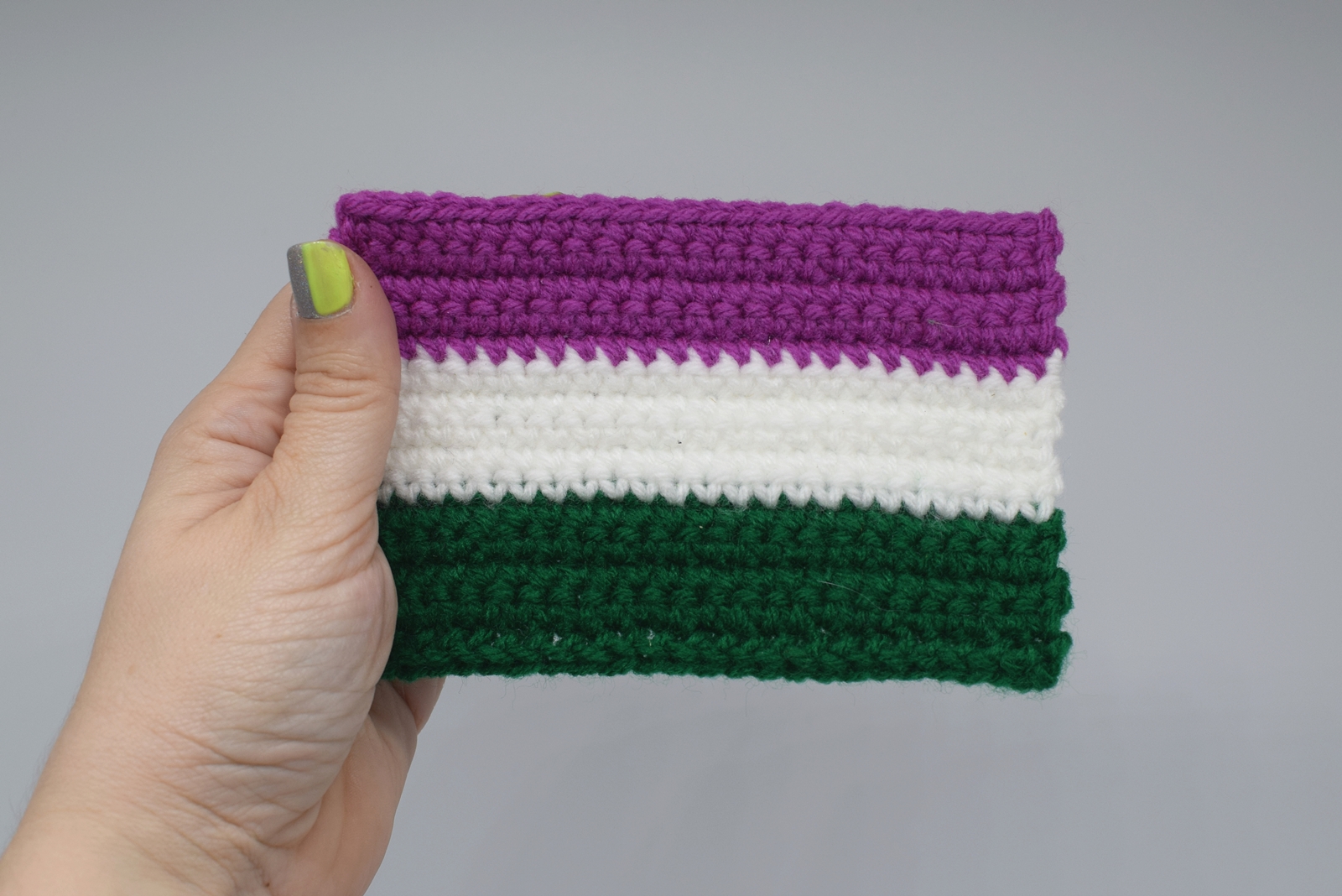 Hand holding Mini Crochet Genderqueer Pride Flag on white background