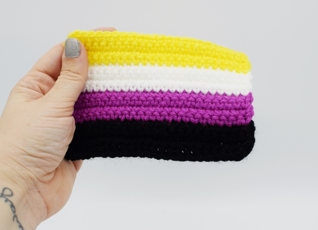 Hand holding a Crochet Non-binary Pride flag on a white background