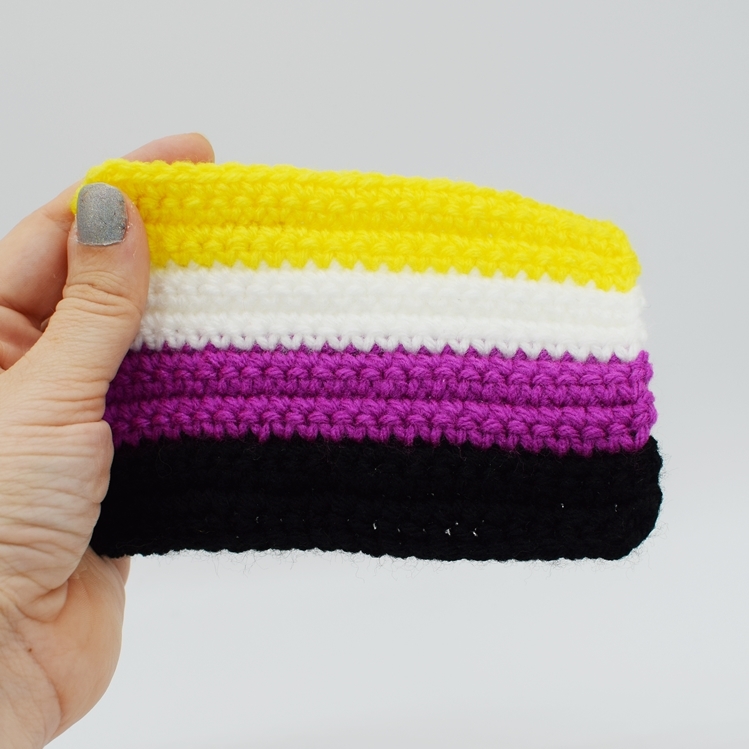 Hand holding a Crochet Non-binary Pride flag on a white background