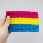 hand holds a crochet pansexual pride flag against a white background