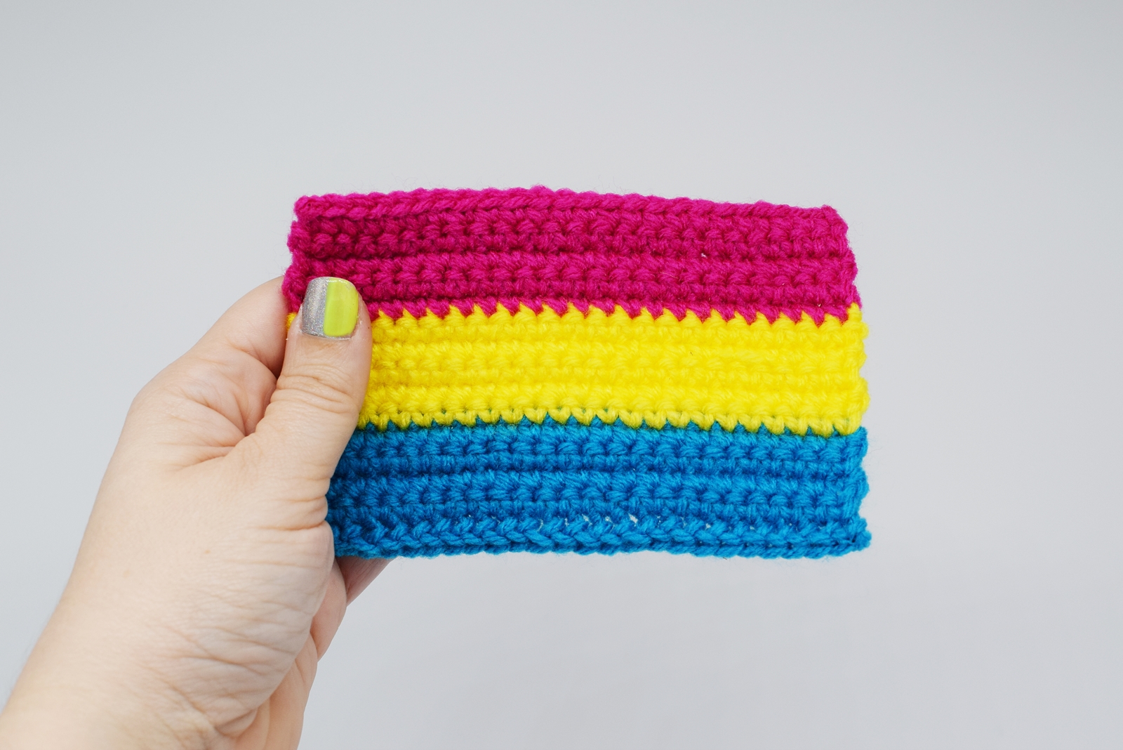 hand holds a crochet pansexual pride flag against a white background