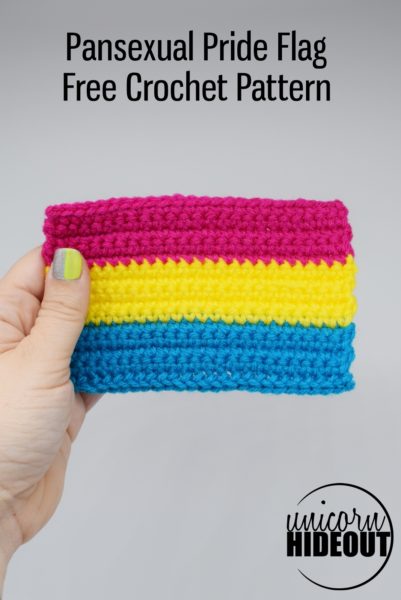 hand holds a crochet pansexual pride flag against a white background, words on image: "Pansexual Pride Flag Free Crochet Pattern, Unicorn Hideout"