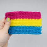 hand holds a crochet pansexual pride flag against a white background