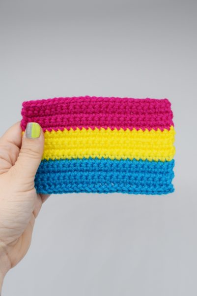 hand holds a crochet pansexual pride flag against a white background