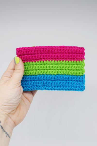 Hand holding Crochet polysexual pride flag on a white background