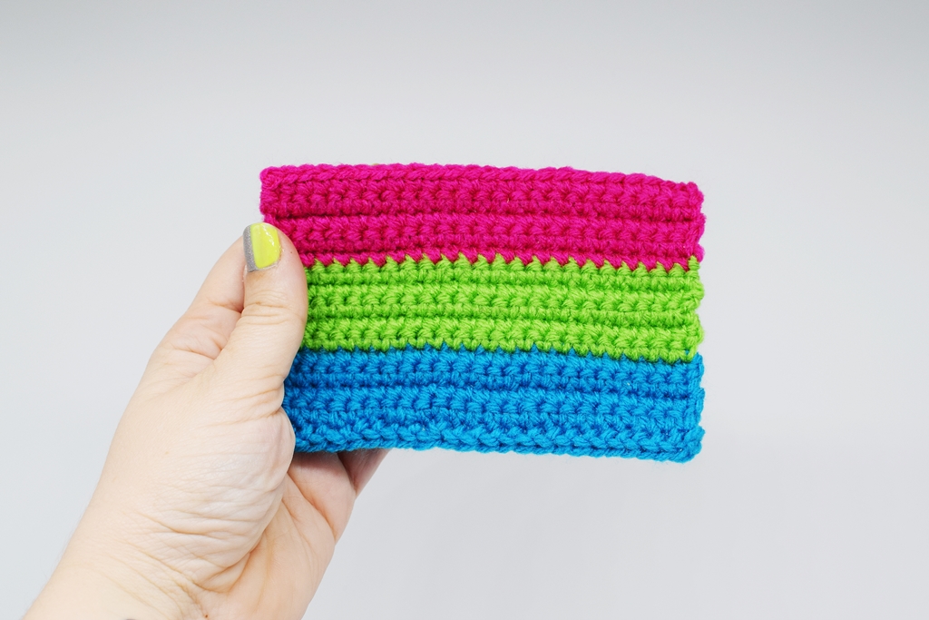 Hand holding Crochet polysexual pride flag on a white background