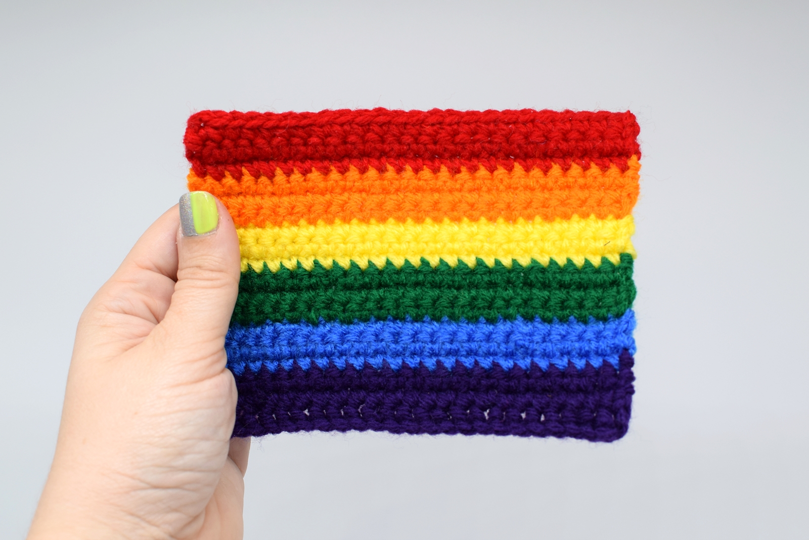 hand holds a mini rainbow Pride flag against a white background