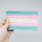 Hand holds a small crochet transgender Pride flag against white background