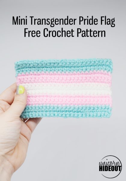 Hand holds a small crochet transgender Pride flag against white background, words on image say "Mini Transgender Pride Flag Free Crochet Pattern Unicorn Hideout"