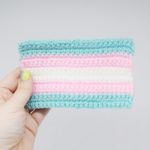 Hand holds a small crochet transgender Pride flag against white background