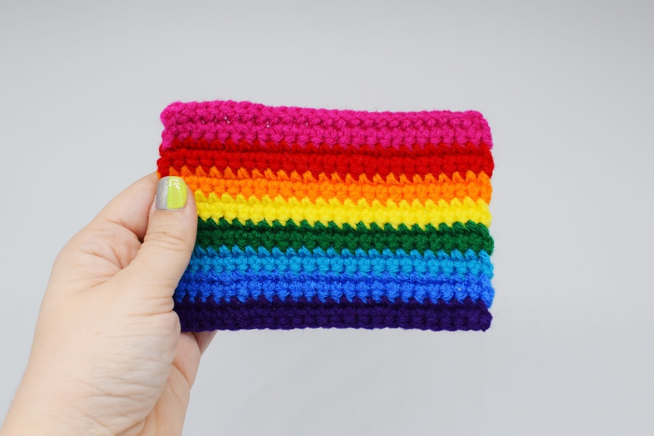 hand holds a mini rainbow Pride flag against a white background