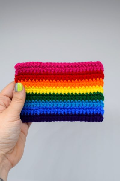 hand holds a mini rainbow Pride flag against a white background