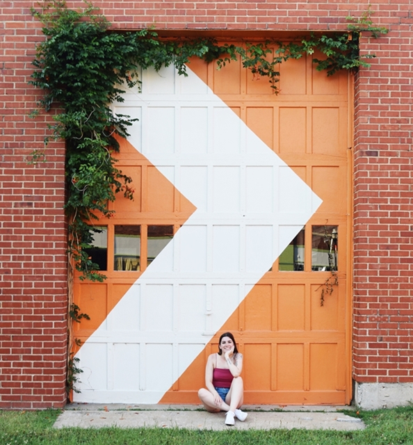 Orange garage door with a white chevron, a woman sits in front of it