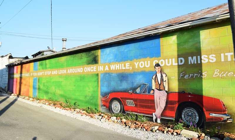 Mural that covers a long wall in bright colors, with a red convertible and life size Ferris Bueller