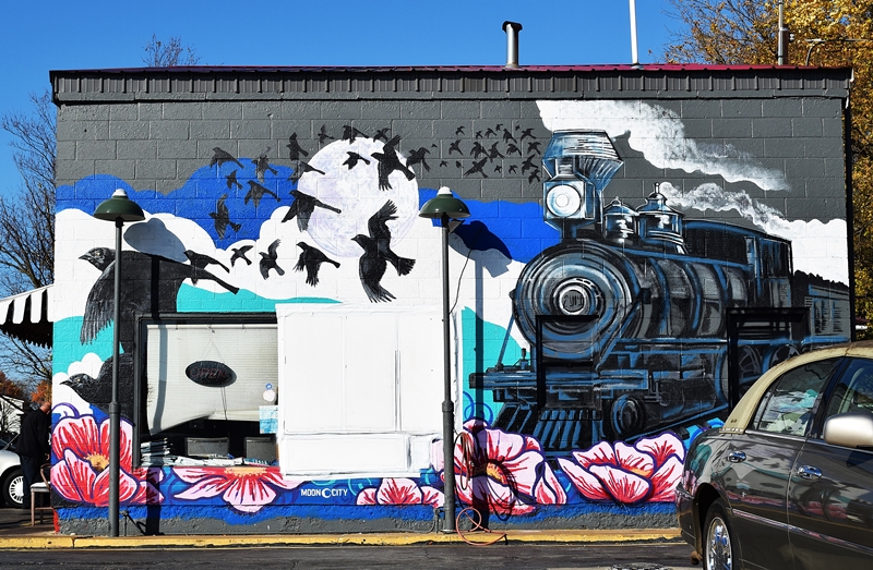 Mural covering the side of a buidling with an old fashioned train, birds and flowers