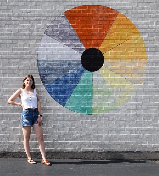 Woman stands to the left of a large color wheel mural