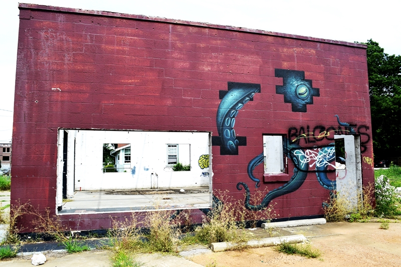 Mural of an octopus peeking out from behind bricks on an abandoned building