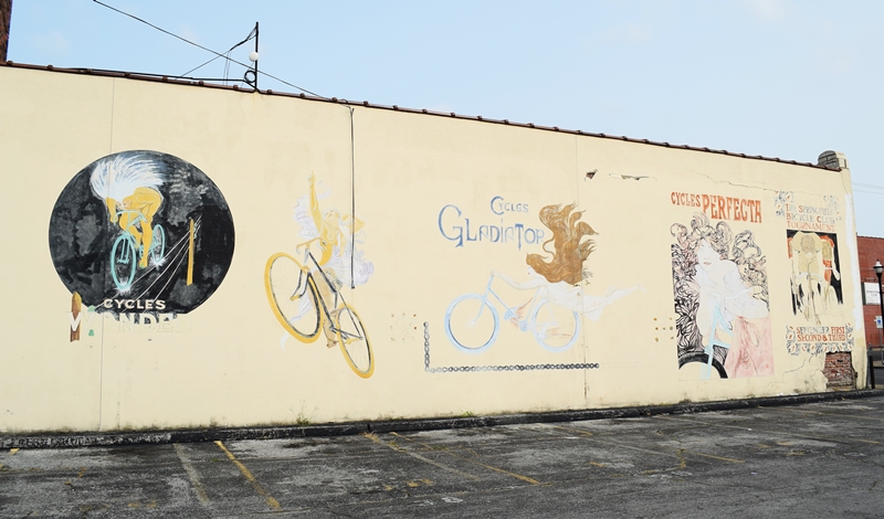 Old cycling murals on the side of a light brick building