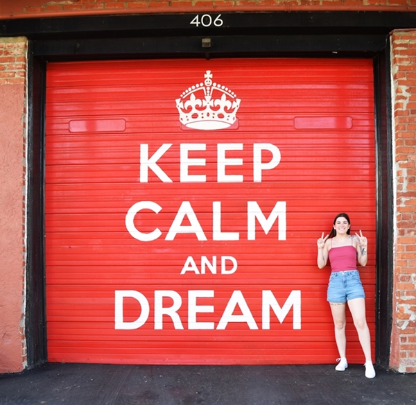 Red garage door with Keep Calm and Dream written on it, a woman stands to this side throwing peace signs