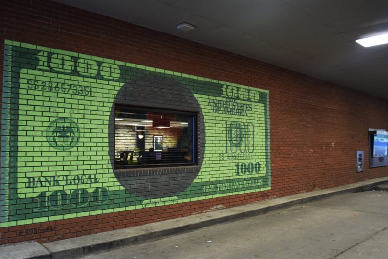 Thousand dollar bill painted on a brick wall with a bank window in the middle