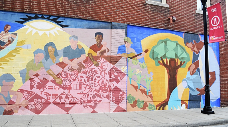 Mural of people sitting around a table on the side of a brick building