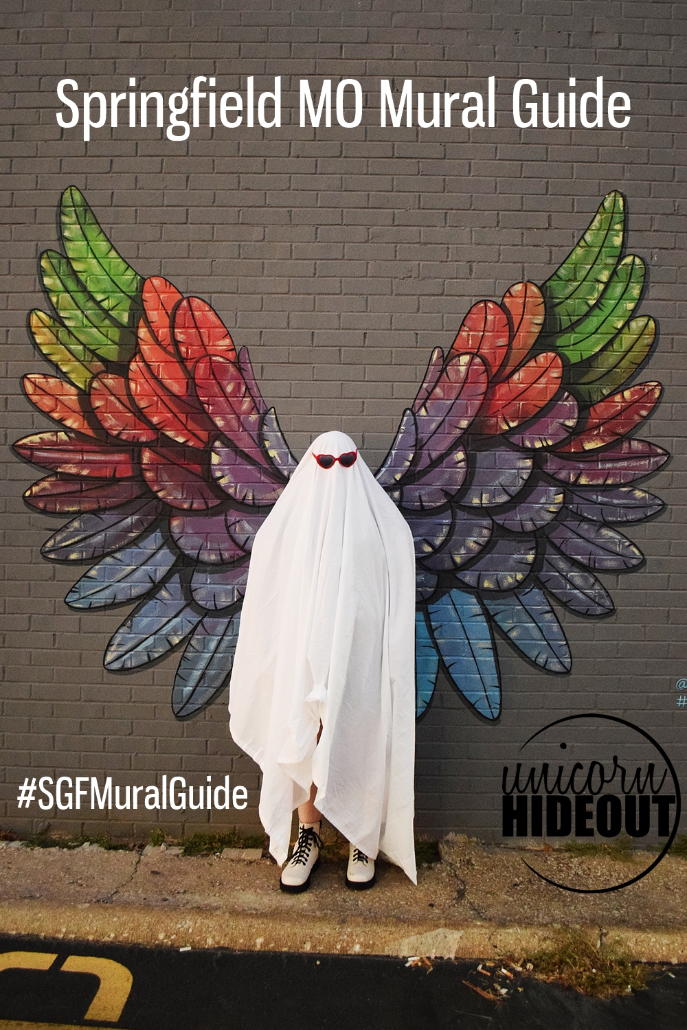 Person in a ghost costume in front of rainbow wings, words on the image say "Springfield MO Mural Guide, #SGFMuralGuide, Unicorn Hideout"