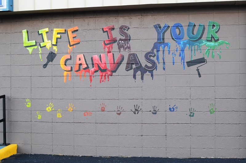 mural painted on a gray wall says Life If Your Canvas with paint drips