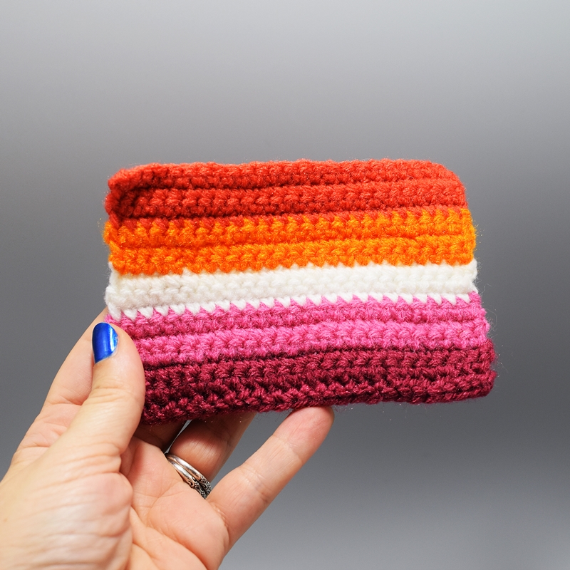 hand holding a small crocheted lesbian pride flag