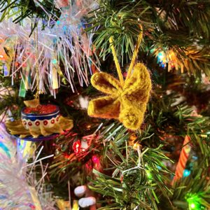 Gold crochet crab rangoon ornament hangs from a branch of a Christmas tree with colored lights and white tinsel.