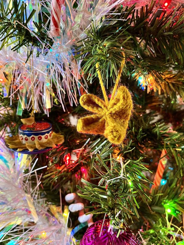 Gold crochet crab rangoon ornament hangs from a branch of a Christmas tree with colored lights and white tinsel.